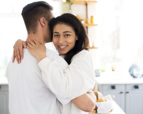 ethnic-young-female-hugging-boyfriend-looking-camera